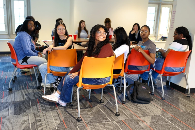 A student smiles in the middle of a group of students discussing their research